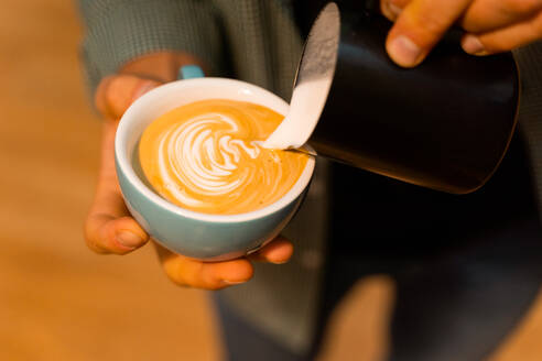 Hohe Winkel von unerkennbar Ernte Barista Zugabe von Milch in Tasse mit Kaffee bei der Vorbereitung leckeren Cappuccino - ADSF23010