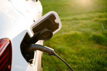 From above of electric ecologic car recharging parked on road near green field on sunny day - ADSF23013