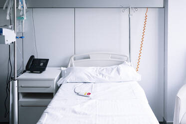 Leeres Bett mit Schwesternrufknopf in der Nähe des Infusionsständers in einer hell ausgestatteten Station in einem modernen Krankenhaus - ADSF23036