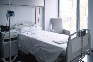 Leeres Bett mit Schwesternrufknopf in der Nähe des Infusionsständers in einer hell ausgestatteten Station in einem modernen Krankenhaus - ADSF23042