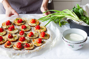 High angle of crop anonymous cook standing at table with plate of homemade baked appetizers made of eggplant mozzarella and cherry tomatoes with onion - ADSF23083