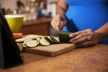 Frau schneidet Zucchini auf einem Holzbrett in der Küche - PMF01758