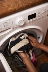 Mature woman loading clothes in washing machine at home - PMF01760