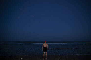 Mann in Badeshorts steht in der Morgendämmerung am Wasser - PMF01763