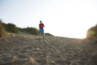 Männlicher Sportler läuft bei Sonnenaufgang auf einer Sanddüne - PMF01767