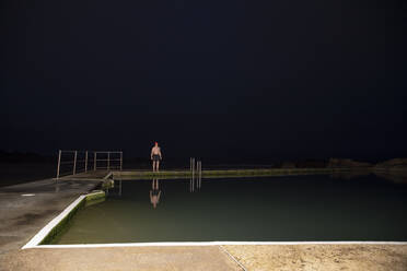 Sportsman standing at poolside during dawn - PMF01768