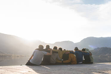 Männliche und weibliche Freunde, die an einem sonnigen Tag auf der Promenade sitzen und sich umarmen - JAQF00503