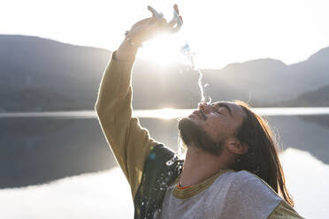 Mann gießt Wasser über das Gesicht an einem sonnigen Tag - JAQF00505