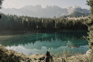 Paar sitzt auf einer Felsformation am Karersee inmitten von Bäumen in Südtirol, Italien - MJRF00380