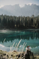 Couple sitting on rock at Carezza lake in South Tyrol, Italy - MJRF00384