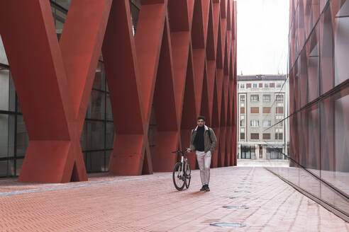 Männlicher Fachmann, der ein Fahrrad vor einem Bürogebäude in der Stadt fährt - JAQF00515