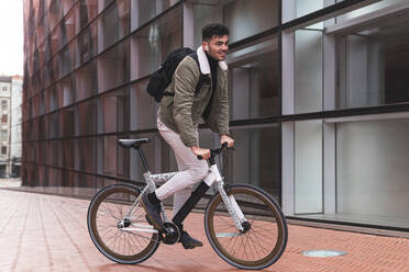 Male professional with backpack riding bicycle outside office building - JAQF00520