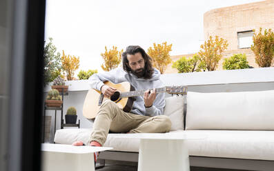 Mann mit langen Haaren spielt Gitarre auf dem Balkon - JCCMF01932