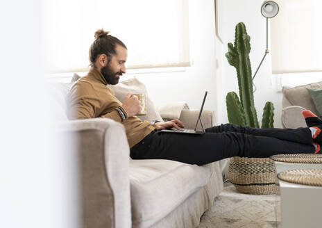 Entspannter Mann mit Tablet-PC auf dem Sofa im heimischen Wohnzimmer - JCCMF01956