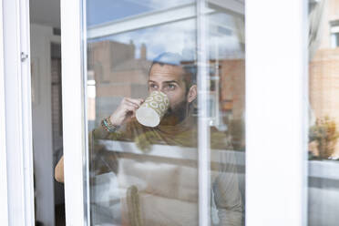 Mann, der Kaffee trinkt und durch ein Fenster schaut, gesehen durch Glas - JCCMF01959