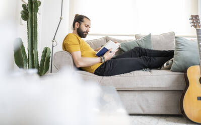 Mann liest ein Buch und entspannt sich auf dem Sofa zu Hause - JCCMF01969