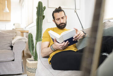 Mann in Freizeitkleidung liest zu Hause ein Buch - JCCMF01970