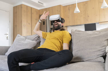 Cheerful man with virtual reality headset at home - JCCMF01973