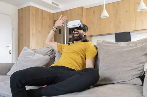 Fröhlicher Mann mit Virtual-Reality-Headset zu Hause - JCCMF01973