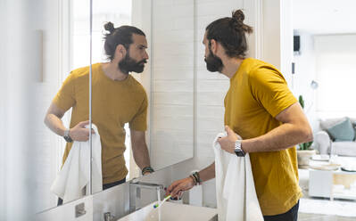 Hübscher Mann wäscht Zahnbürste, während er in den Spiegel schaut - JCCMF01975
