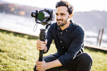 Handsome man holding gimbal looking through camera on sunny day - DAWF01881