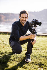 Smiling handsome man holding gimbal on sunny day - DAWF01882