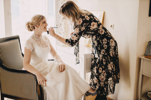 Make-up artist applying lipstick on excited bride during wedding - DAWF01893