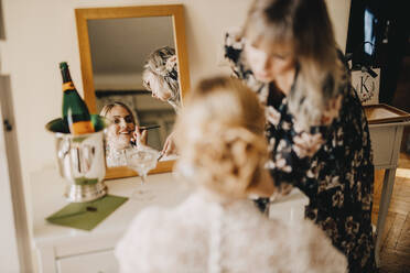 Die Braut schaut in den Spiegel, während die Kosmetikerin das Make-up für die Hochzeit aufträgt - DAWF01894