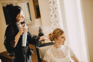 Friseur hält Haarspray Flasche, während schöne Braut sitzt in Hochzeitskleid - DAWF01895