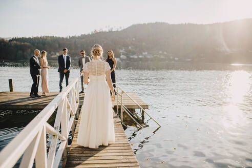 Bride walking on jetty towards groom and friends - DAWF01903