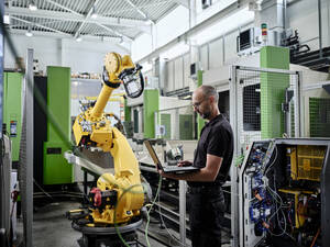 Male engineer using laptop by robotic arm - CVF01747