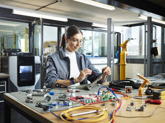 Smiling female engineer working with electrical component in industry - CVF01748