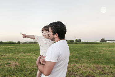 Mann, der einen kleinen Jungen trägt, während er im Gras steht - FLMF00407