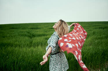 Smiling woman holding scarf on grass - KIJF03736