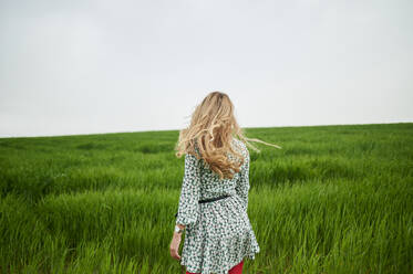 Blonde Frau geht auf einer Wiese im Gras - KIJF03738