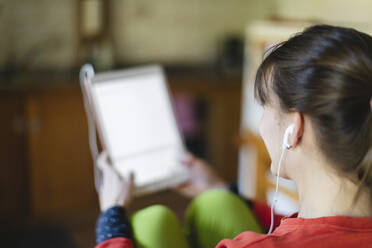 Frau mit In-Ear-Kopfhörern und digitalem Tablet zu Hause - MCVF00772