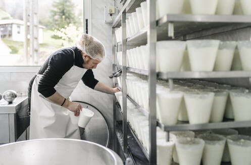 Reifer männlicher Unternehmer ordnet Käsebehälter in einem Regal im Lagerraum - DGOF02129