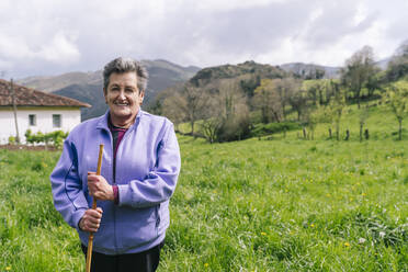 Lächelnde aktive ältere Frau mit Gehstock im Gras stehend - DGOF02142