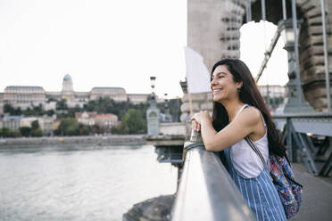 Lächelnde Frau, die wegschaut und sich auf ein Brückengeländer stützt - ABZF03543