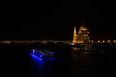Beleuchtetes Passagierschiff mit dem Gebäude des ungarischen Parlaments in Budapest, Ungarn - ABZF03548