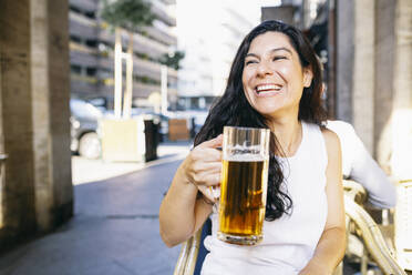 Happy mid adult woman having drink at beer garden - ABZF03550