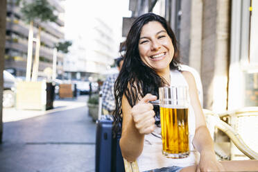 Smiling woman holding drink glass while sitting at beer garden - ABZF03551