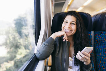 Mid adult woman sitting with hand on chin in train - ABZF03570