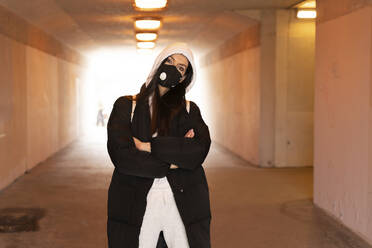 Woman wearing face mask and hood clothing standing with arms crossed in underground - SPCF01343