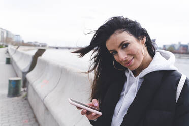 Smiling woman staring while holding mobile phone - SPCF01348