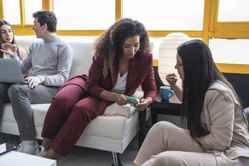 Geschäftsfrauen diskutieren über Handy mit Kollegen im Coworking-Büro - SNF01227