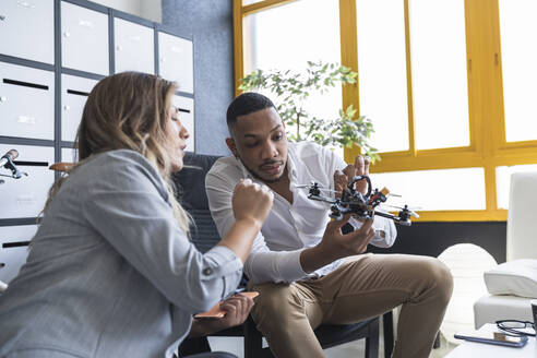 Businessman explaining drone model to female colleague in coworking office - SNF01233