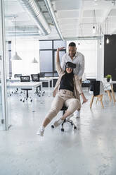 African businessman standing behind smiling female colleague wearing virtual reality simulator in coworking office - SNF01242