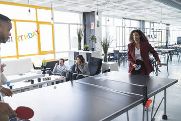 Lächelnde Geschäftsfrau spielt Tischtennis mit einem männlichen Kollegen in einem Coworking-Büro - SNF01245