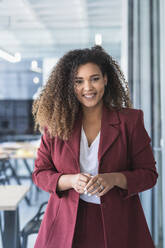 Smiling curly haired businesswoman standing in coworking office - SNF01246